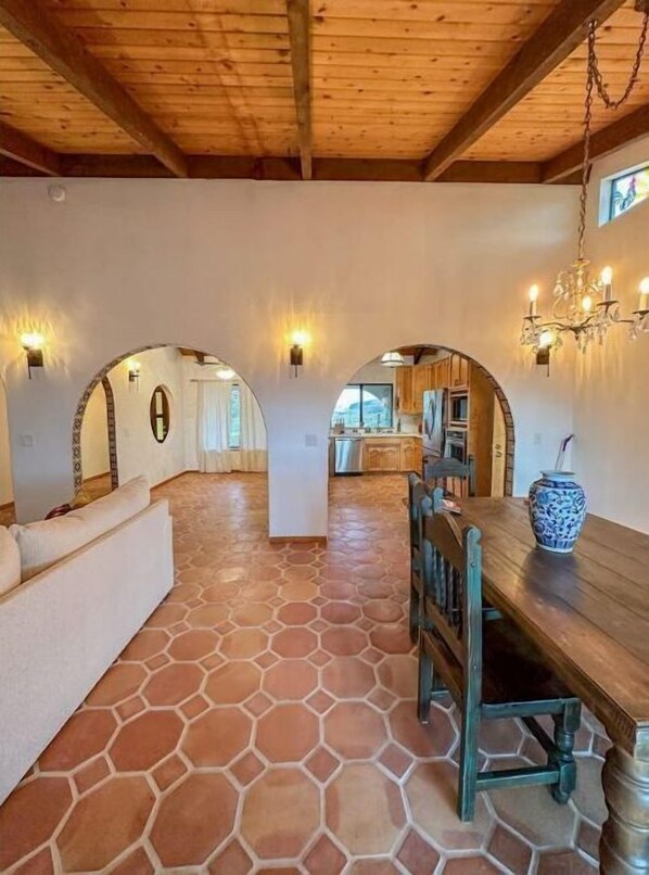 A spacious interior with a stone-tiled floor, wooden ceiling beams, and a dining area with a wooden table and chairs.