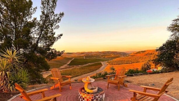 A patio with four Adirondack chairs and a fire pit, overlooking a scenic landscape.