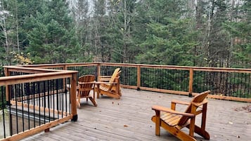 Relax on the deck surrounded by a dense forest, with Adirondack chairs inviting you to unwind.