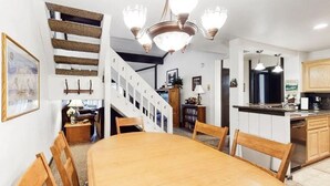 A dining area with a wooden table and chairs, a staircase with a railing, and a kitchen with wooden cabinets and a countertop. - The Summit 66 Walk to Eagle Lodge Chair 15 (Mammoth Lakes)