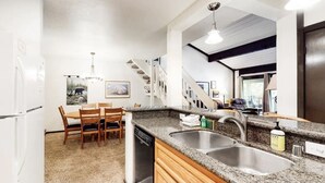 A modern kitchen with granite countertops, stainless steel sinks, and a dishwasher. There is a dining area with wooden chairs and a table. - The Summit 66 Walk to Eagle Lodge Chair 15 (Mammoth Lakes)