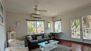 Un salon spacieux avec une grande fenêtre, un ventilateur de plafond et une table basse blanche.