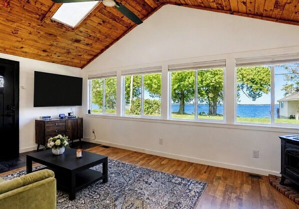 Un salon spacieux avec un plafond haut, de grandes fenêtres, un téléviseur à écran plat, une table basse en bois foncé et une cheminée.