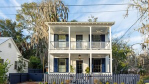 Une maison blanche à deux étages, dotée d’un balcon, d’une clôture en piquets et d’une allée gravillonnée.