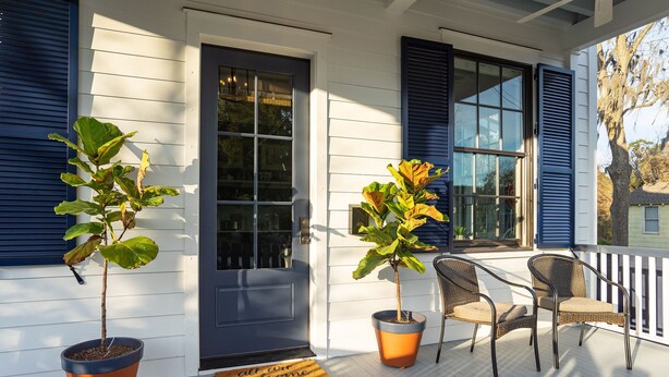 Une véranda avec deux plantes en pot, une porte et deux fauteuils en osier.