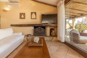 A cozy living room with a fireplace, a sofa, a coffee table with decorative items, and a TV mounted above the fireplace. - LUNA BAY HOME RETREAT with a view of Porto Luna Bay, 2 km from Villasimius (VILLASIMIUS)
