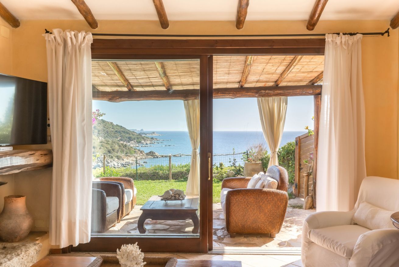 Une pièce dotée d’une grande porte-fenêtre coulissante donnant sur une terrasse aménagée avec du mobilier d’extérieur et offrant une vue sur la mer.