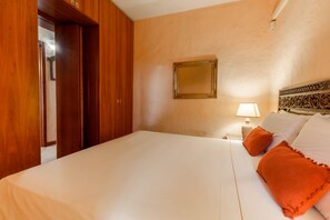 A hotel room with a large bed, wooden wardrobe, a nightstand with a lamp, and a decorative headboard. - LUNA BAY HOME RETREAT with a view of Porto Luna Bay, 2 km from Villasimius (VILLASIMIUS)