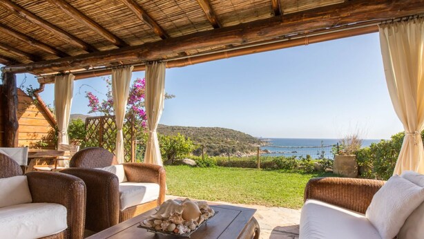 Un espacio de estar techado al aire libre con mobiliario de mimbre y una mesa decorada con conchas.