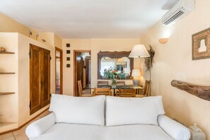 A cozy room with a white sofa, a dining table with chairs, a mirror, and a wooden door.