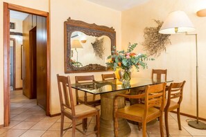 A dining area with a glass-top table, wooden chairs, a vase with flowers, a mirror, and a floor lamp. - LUNA BAY HOME RETREAT with a view of Porto Luna Bay, 2 km from Villasimius (VILLASIMIUS)