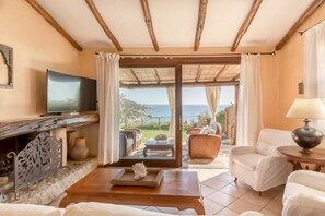 Una sala de estar acogedora con televisión, asientos cómodos, chimenea y vista al mar.