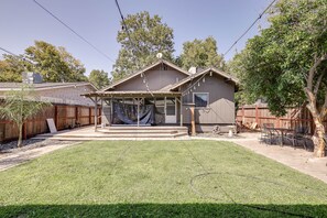 Ein Haus mit überdachter Terrasse, umzäunter Garten und Baum.