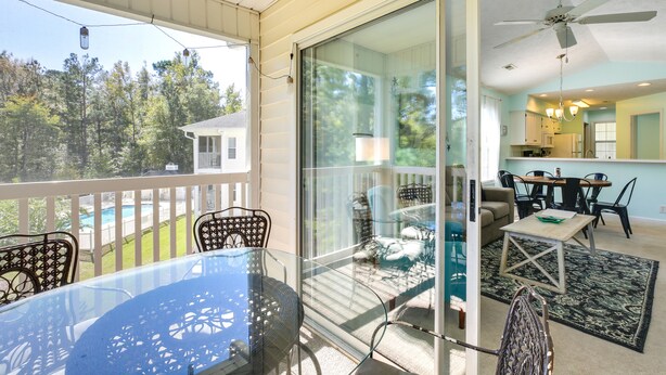 A glass-enclosed balcony with a table and chairs, a view of a swimming pool, and a kitchen area visible through the glass. - Golf & Resort Perks: Premier Condo 10 mi to Myrtle (Longs)