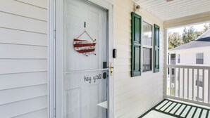 A white door with a glass panel and a welcome sign, a green window shutter, and a white porch with a green mat. - Golf & Resort Perks: Premier Condo 10 mi to Myrtle (Longs)
