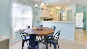 A dining area with a round wooden table surrounded by chairs, a chandelier, and a window with curtains. - Golf & Resort Perks: Premier Condo 10 mi to Myrtle (Longs)