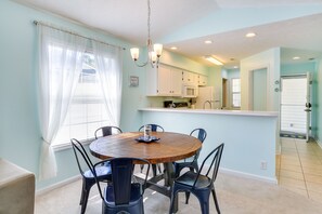 A dining area with a round wooden table surrounded by chairs, a chandelier, and a window with curtains. - Golf & Resort Perks: Premier Condo 10 mi to Myrtle (Longs)