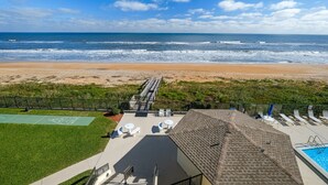A beach view from a hotel balcony with a pool, sun loungers, and a shuffleboard court.