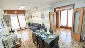 Un comedor con una mesa lista para cuatro personas, un sofá y una zona de cocina con estufa y fregadero.