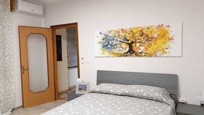 Un dormitorio con una cama, una mesita de noche, un cuadro enmarco y una puerta.