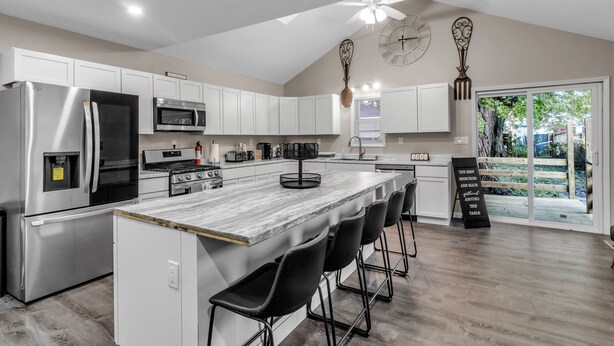A modern kitchen with white cabinets, stainless steel appliances, a large island with bar stools, and a ceiling fan. - The Davey Retreat (Buffalo)