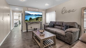 A living room with a large flat-screen TV, a brown leather sofa, a wooden coffee table, and a wall with the word "love" above a mirror. - The Davey Retreat (Buffalo)