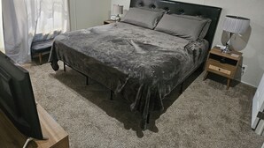 Ein Schlafzimmer mit einem Bett, Nachttischen, einer Lampe, einem Fernseher und einem Bild an der Wand.