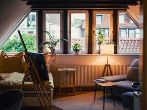 Ein gemütliches Zimmer mit schrägem Dach, einem Bett, einem Schreibtisch, einem Stuhl und einer Heizung.