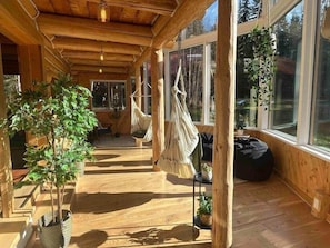 En stuga med träinredning, en hängmatta, krukväxter och stora fönster.