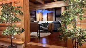 A wooden cabin interior with a staircase leading to a living area, featuring two potted plants and a sofa. - Family Cabin + Games Barn | Hot Tub | Theatre (Columbia-Shuswap)