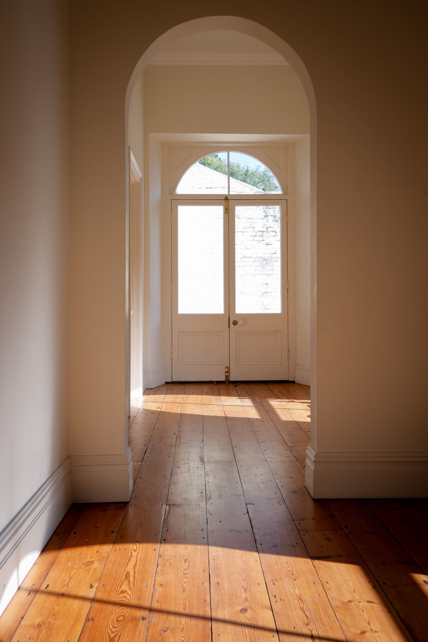 A hallway with wooden flooring leading to a white door with a glass panel.