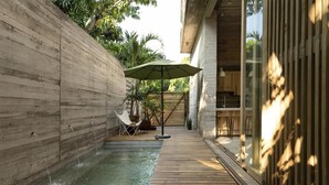 Een zwembad buiten met moderne inrichting, een houten terras, een ligstoel, een tafel en een grote parasol.