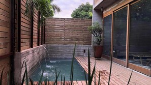 A wooden deck with a small rectangular pool, a wooden fence, and a potted plant.