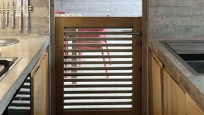 Una cocina estrecha con armarios de madera, un lavamanos de acero inoxidable y una ventana con persianas.