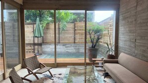 Una sala de estar moderna con puerta de vidrio que da a un patio trasero con piscina, cerca de madera y plantas en macetas.