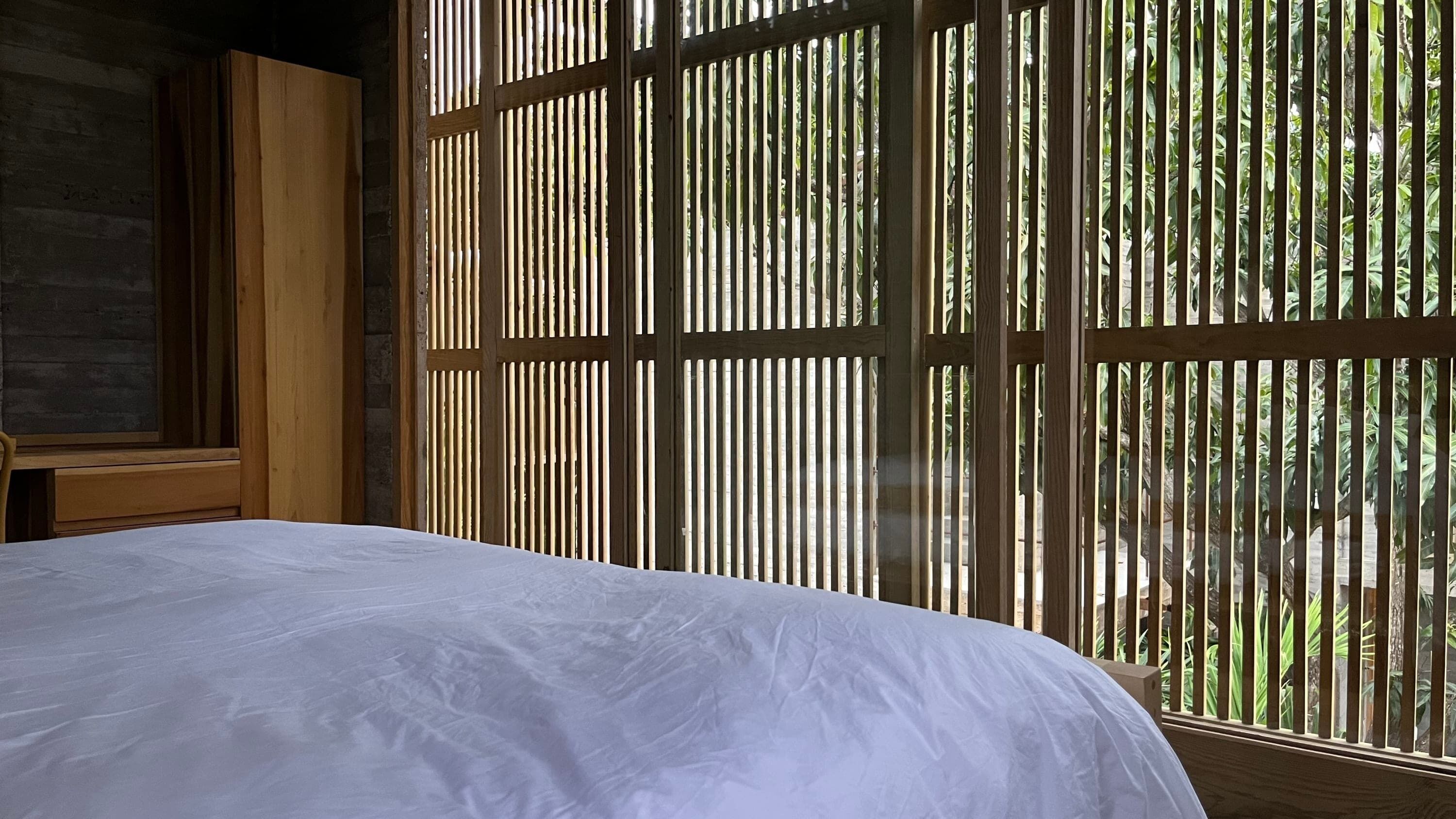 A bedroom with a bed, wooden walls, and a window with vertical blinds.