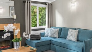 A modern living room with a teal sofa, a wooden coffee table, and a fireplace. - Firgarth Lodge  - sleeps 6 guests  in 3 bedrooms (Windermere)