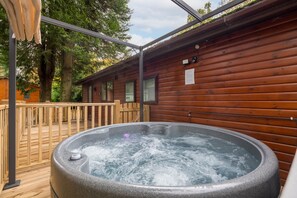 Een hottub in een houten blokhut met een houten terras en een pergola.