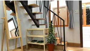 Staircase with a wooden shelf and framed picture, set against a tiled floor and window with curtains.