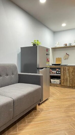 Cozy living space with a sofa, kitchenette, and potted plant.