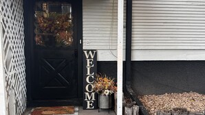 A house entrance with a black door, a welcome sign, and a small flower arrangement on the porch.
