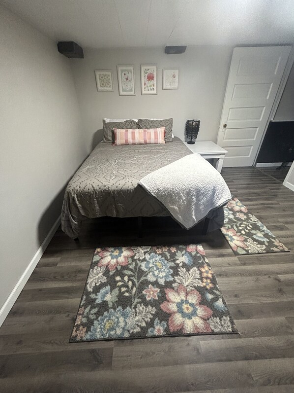 A bedroom with a bed, a nightstand, a door, and a wall with four framed pictures.