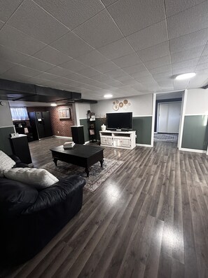 A living room with a black leather sofa, a coffee table, a flat-screen TV, and a white cabinet.