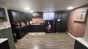 A modern kitchen with dark cabinets, a stainless steel refrigerator, and a wooden floor.