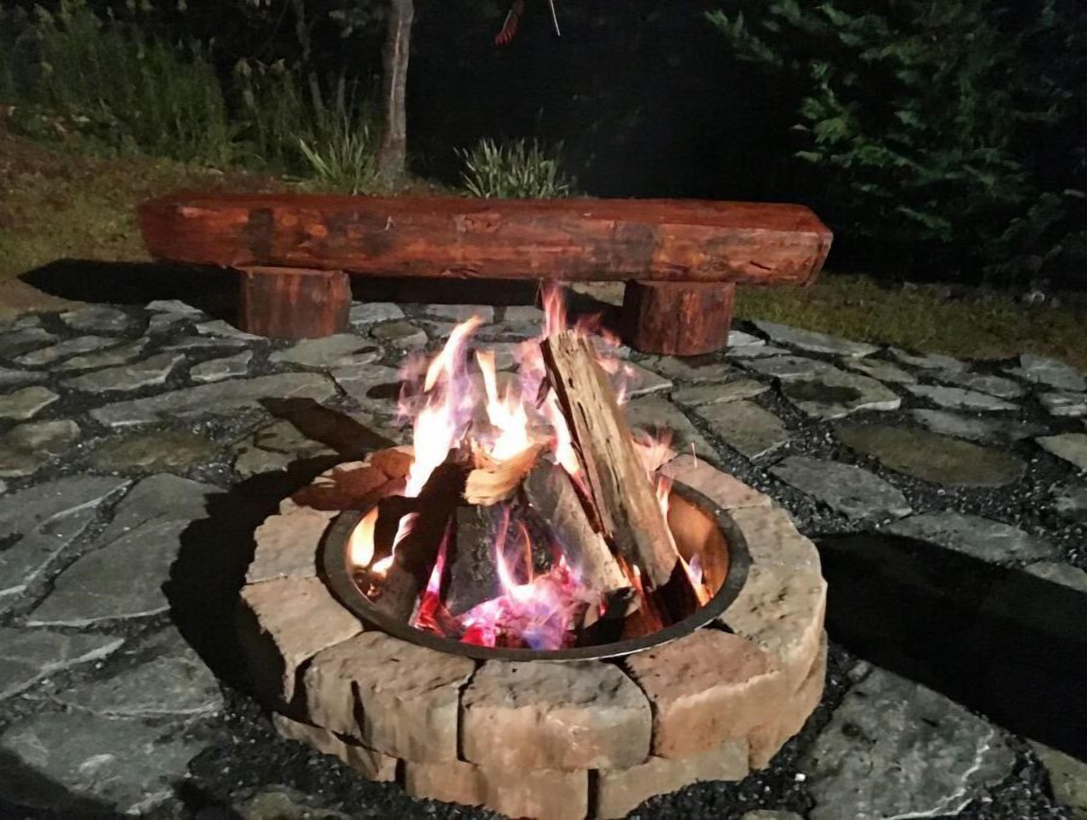 A stone fire pit with burning logs, surrounded by a stone patio.