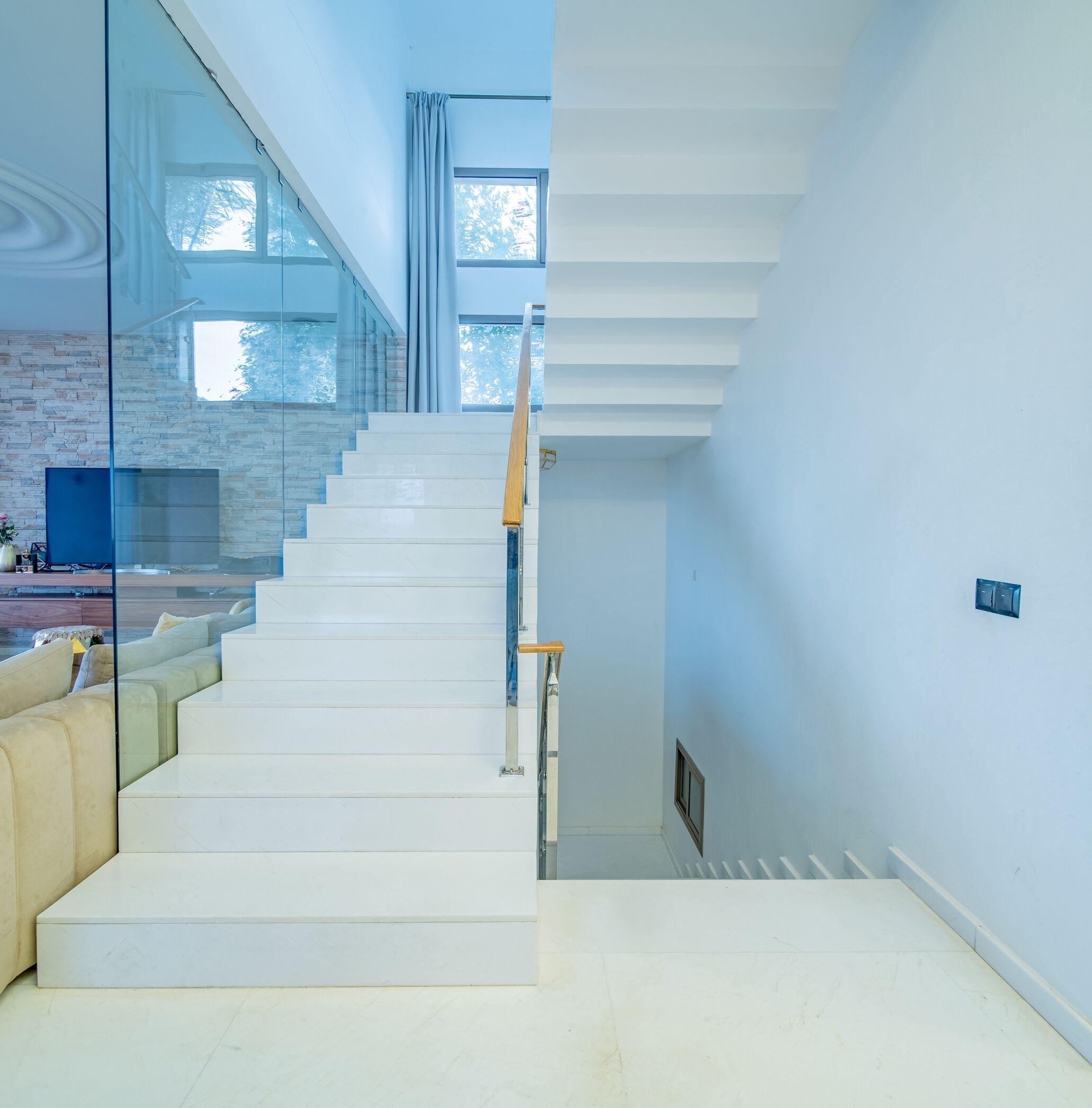 A modern interior with a staircase leading to an upper level, a glass partition, and a seating area with cushions.