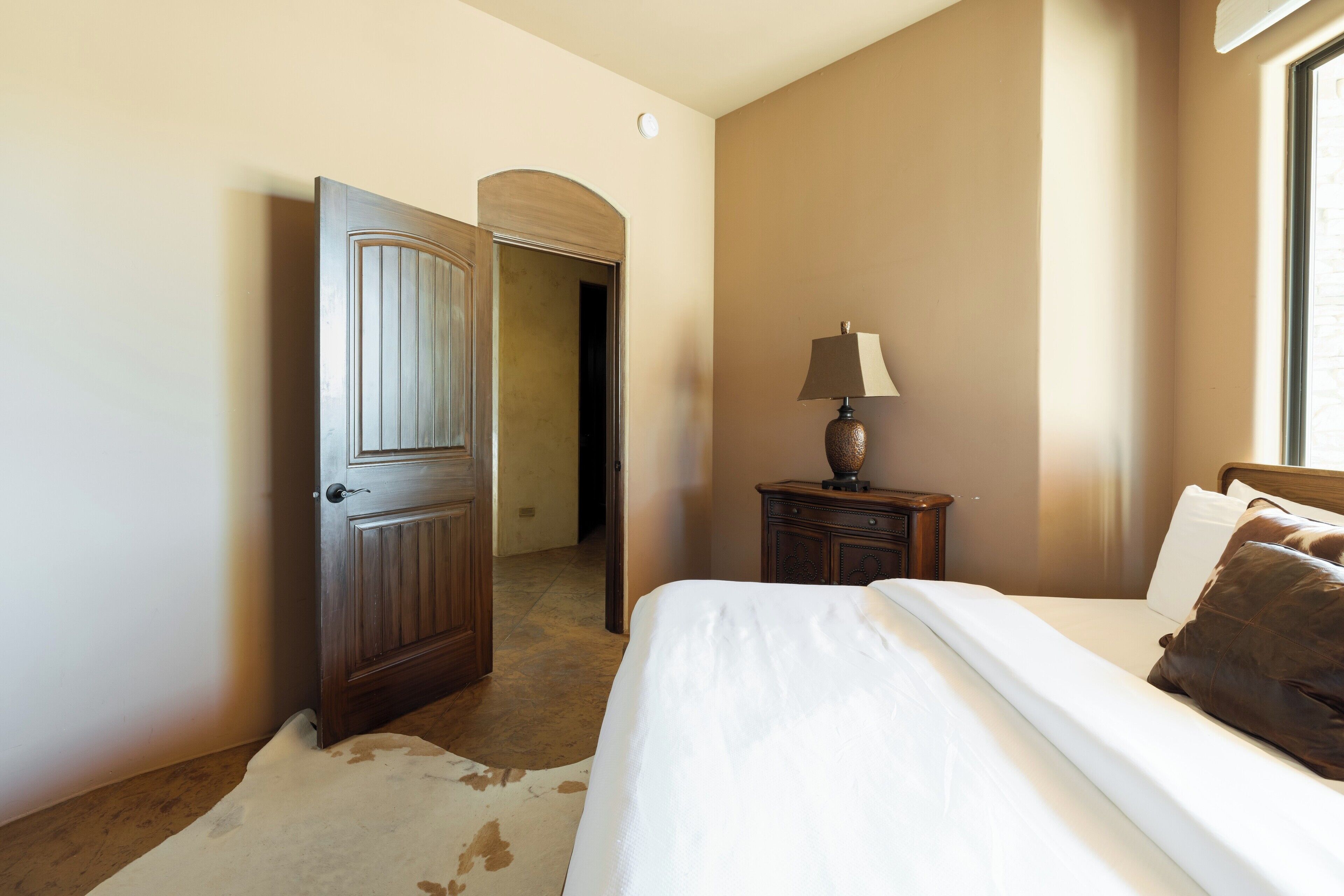 A bedroom with a bed, a nightstand, a lamp, a door, and a cowhide rug.