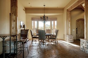 Un comedor con mesa y sillas de madera, una araña y ventanas amplias con vistas al desierto.