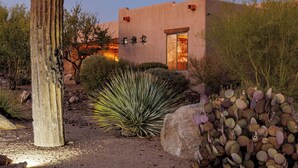 A desert landscape with a large cactus, a building with a door, and a rock formation.