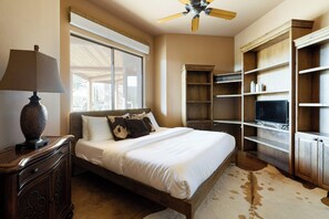 Un dormitorio con cama, ventilador de techo, televisión y estanterías empotradas.